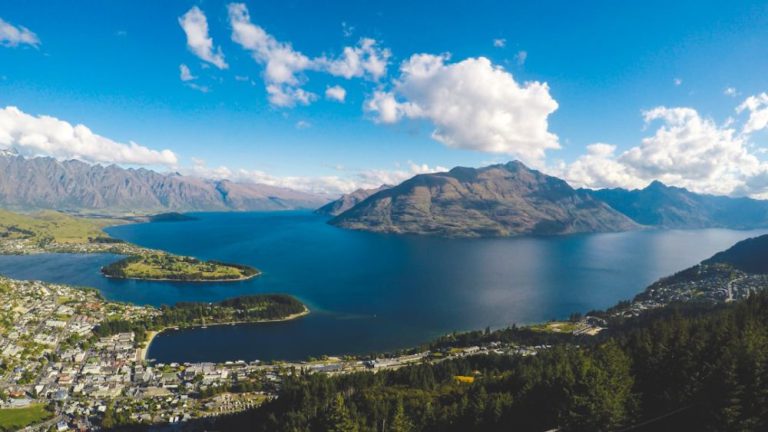 New Zealand - buildings near body of water and mountains under clear blue sky and white clouds at daytime