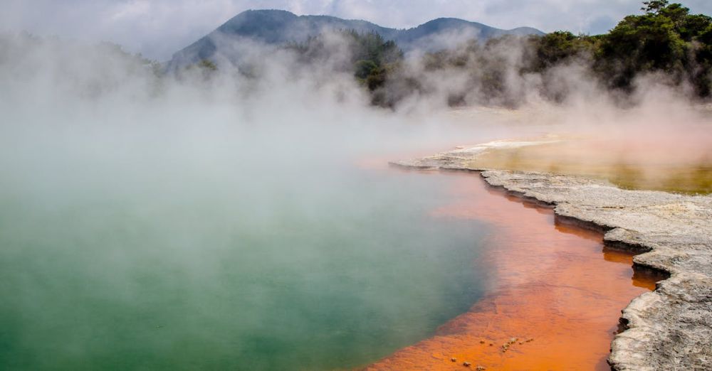 Rotorua - Brown Surface Beside Body of Water in a Distant of Mountains Under White Clouds during Daytime